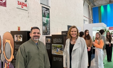 Um homem e uma mulher estão em pé, em uma exposição de fotografia, posando para a foto