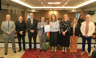 Cinco homens e três mulheres em pé, em uma sala de sessões de julgamento, posam para a foto. Uma mulher e um homem no centro exibem um documento.