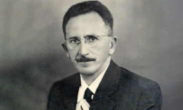 Foto preta e branca de um homem de óculos e bigode