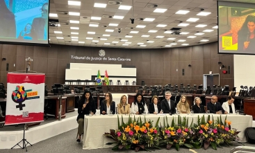 Mesa de autoridades participa de seminário em auditório, com painel do Programa Indira ao lado