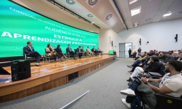 Fotografia de auditório com painel sobre aprendizagem profissional e plateia assistindo.