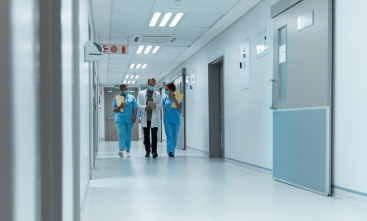 Corredor de hospital com três pessoas vestindo jaleco médico.