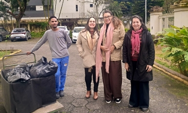 Três mulheres e um rapaz posam para foto ao lado de um carrinho de transporte com sacos pretos
