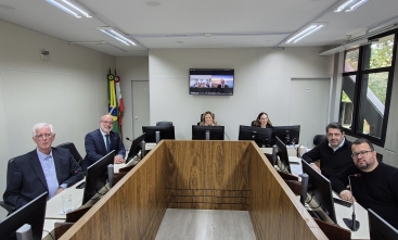 Quatro homens e duas mulheres posam para a foto, sentados ao redor de uma mesa em formato de U
