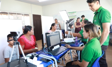 Pessoas participam de um atendimento em uma sala equipada com computadores, câmeras e outros equipamentos tecnológicos.
