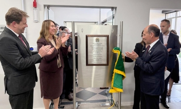 Dois homens de terno e gravata e uma mulher estão aplaudindo felizes em frente a uma placa de inaguração de um forum trabalhista