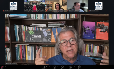 Print de tela com um homem de cabelo grisalho e óculos dando palestra