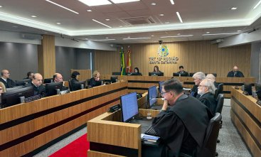 Trezes pessoas vestindo toga sentadas em fileiras de bancadas de madeira, em uma sala de julgamento