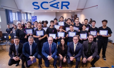 Grupo de jovens recebe certificados durante evento, acompanhado por autoridades e organizadores.