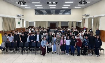 Cerca de cem jovens e adolescentes e outros quatro adultos posam para foto, de pé, em um amplo auditório
