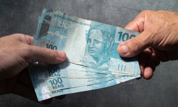 Mão recebe cédulas de 100 reais de outra mão