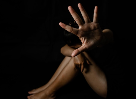 Foto de uma mulher sentada, com foco nas pernas e a palma de uma mão voltada para a câmera