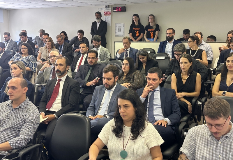 Cerca de 50 pessoas, sentadas e de frente, assistem a uma apresentação em um auditório 