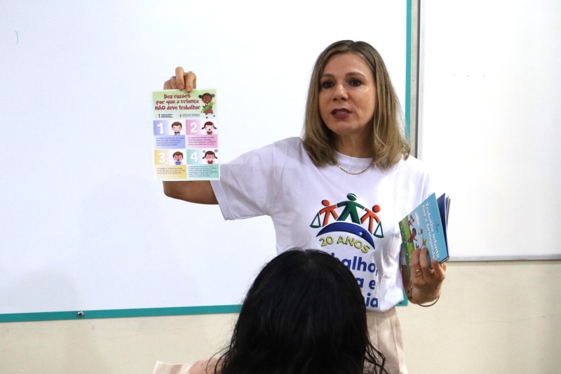 Mulher loira exibe uma cartilha destinada ao público infantil