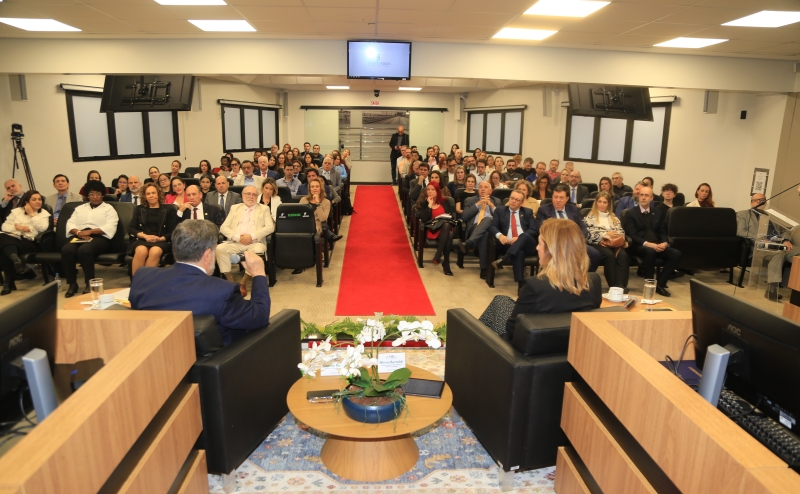 Foto tirada da frente de um plenário mostra cerca de 70 pessoas assistindo a uma palestra
