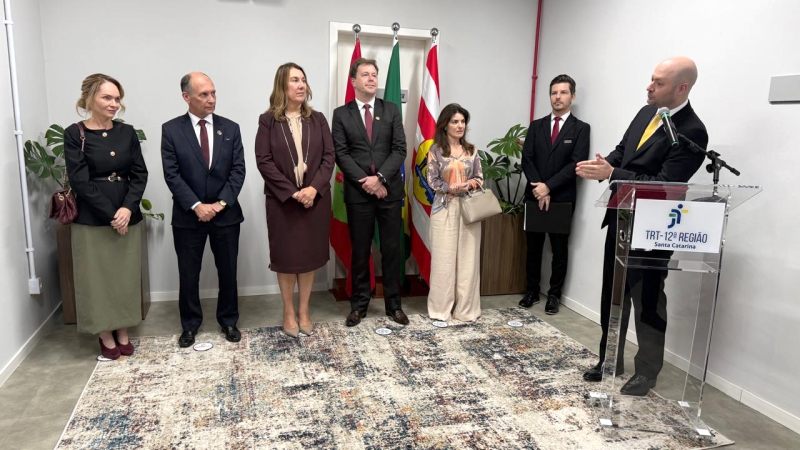 Um homem de terno e gravata está falando em um púlpito e três mulheres e três homens estão em pé ao lado, olhando para ele