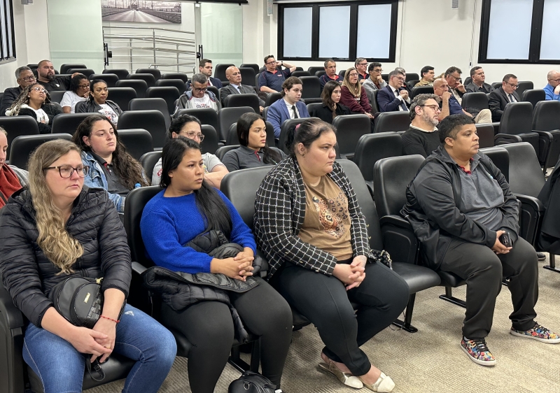 Cerca de 30 pessoas acompanham a sessão em poltronas dentro de uma sala de julgamentos. Em primeiro plano, quatro mulheres