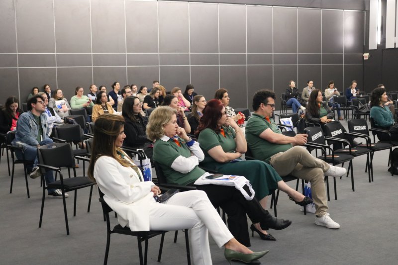 Foto lateral mostra um grupo de cerca de 40 pessoas sentadas em cadeiras