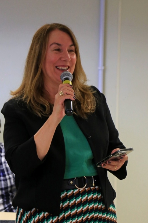 Mulher loira, branca e sorridente fala ao microfone