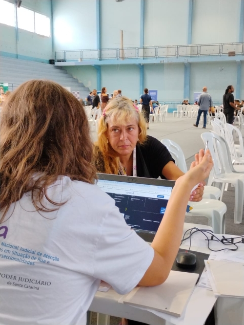 Mulher loira presta atenção à explicação de uma outra mulher, de cabelos castanhos, que está de costas para a foto
