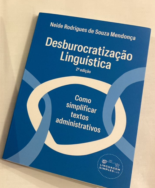 Para todos verem: Texto: "Neide Rodrigues de Souza Mendonça. Desburocratização Linguística. 2ª Edição. Como simplificar textos administrativos. Linguagem Simples Lab”. Ilustração: Capa do livro toda azul com círculos entrelaçados.