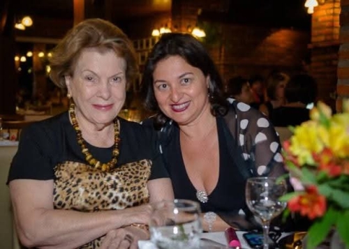 Duas mulheres sentadas à mesa de jantar, em um restaurante, posam para a foto.