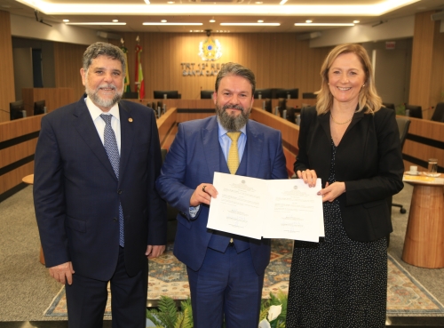 Dois homens e uma mulher posam para a foto. O homem que está no meio exibe dois documentos