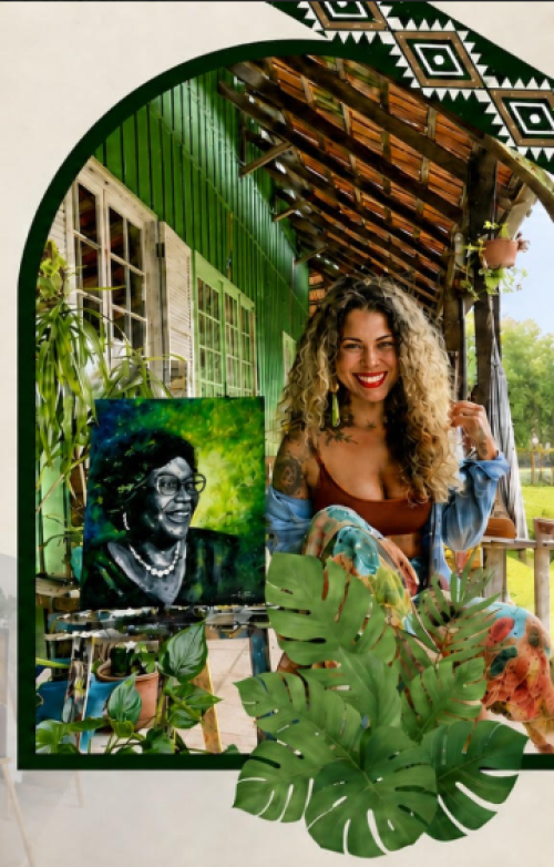 Mulher parda de cabelos cacheados, sorridente, sentada em uma cadeira. Ao lado dela, uma tela de pintura com o rosto de uma mulher negra