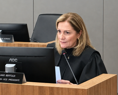 Mulher branca, loira, vestindo toga, fala ao microfone durante uma sessão de julgamento