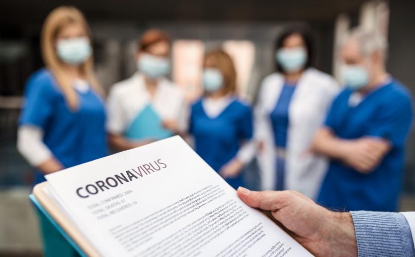Imagem de uma equipe de médicos utilizando máscara de proteçao. À frente, um documento com a palavra coronavírus