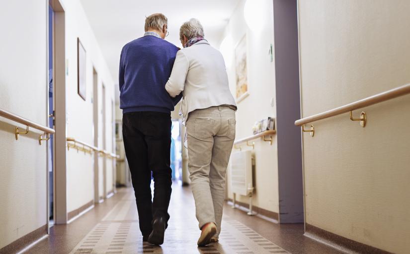 Dois idosos estão de costas andando por um corredor