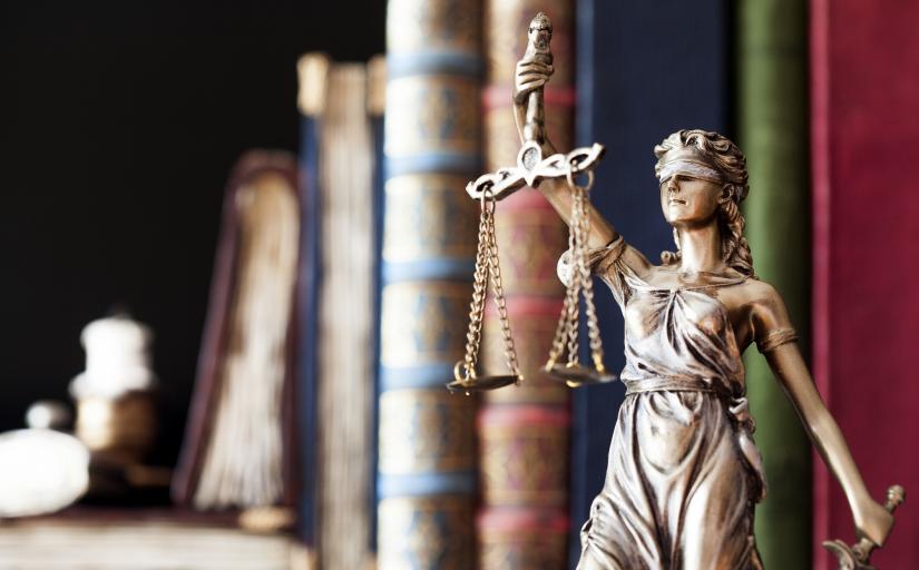Estátua da Justiça ao lado de uma fileira de livros de direito, de diversas cores