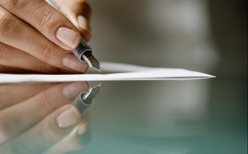 Close de uma mão escrevendo com uma caneta em um papel