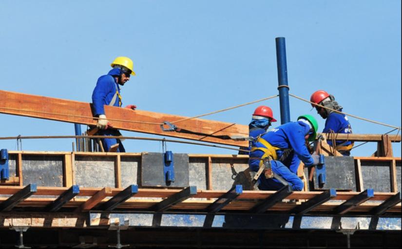 Trabalhadores da construção civil vestidos com EPI em cima de uma lage