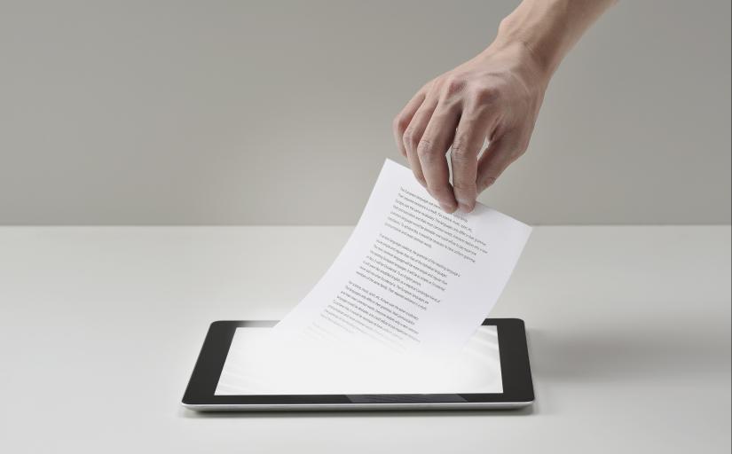 Mão puxa um documento físico de um tablet