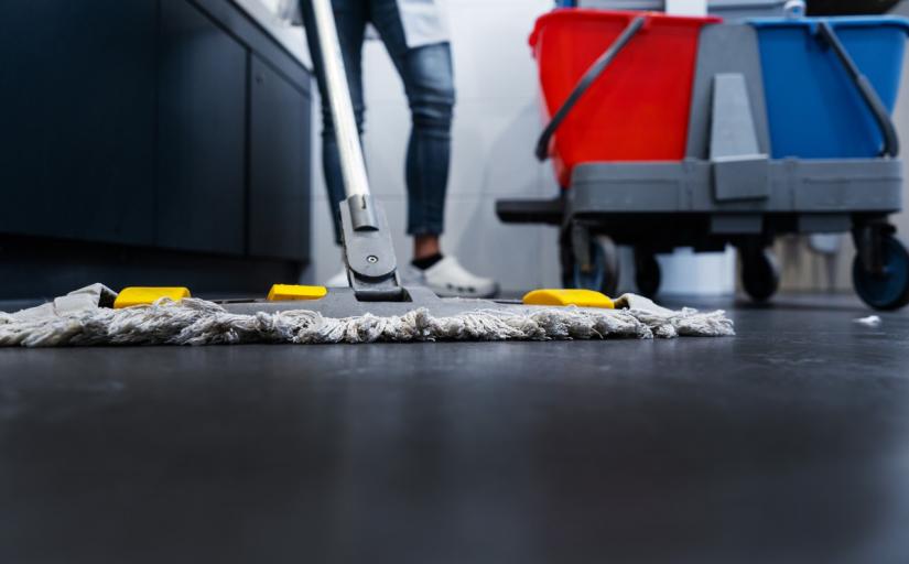 Trabalhadora de limpeza usa escovão e produtos para limpar chão