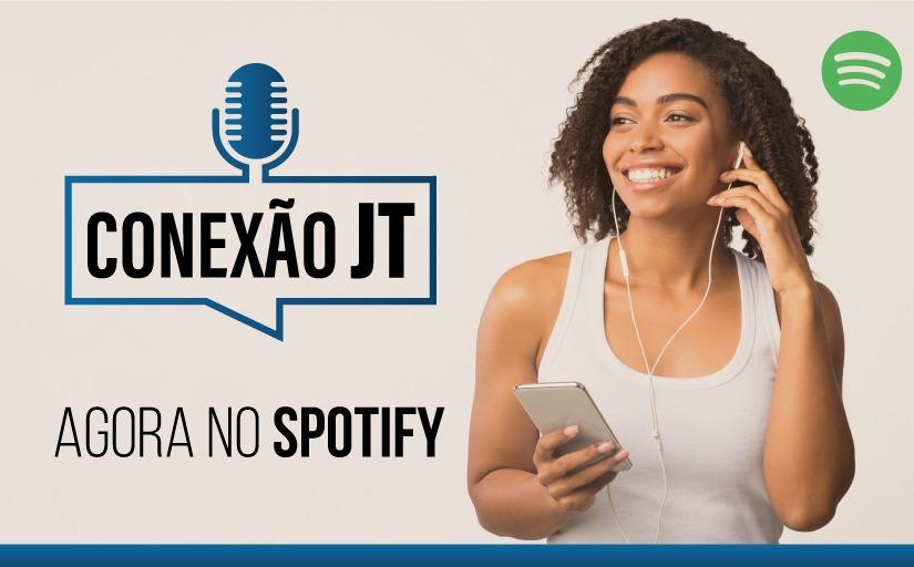 Arte com a foto de uma mulher negra, com fones de ouvido e o celular na mão. Texto: Conexão JT agora no Spotify