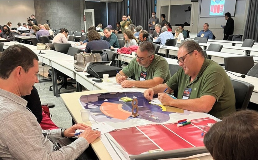 Pessoas divididas em grupos sentadas à mesa e trabalhando em projetos