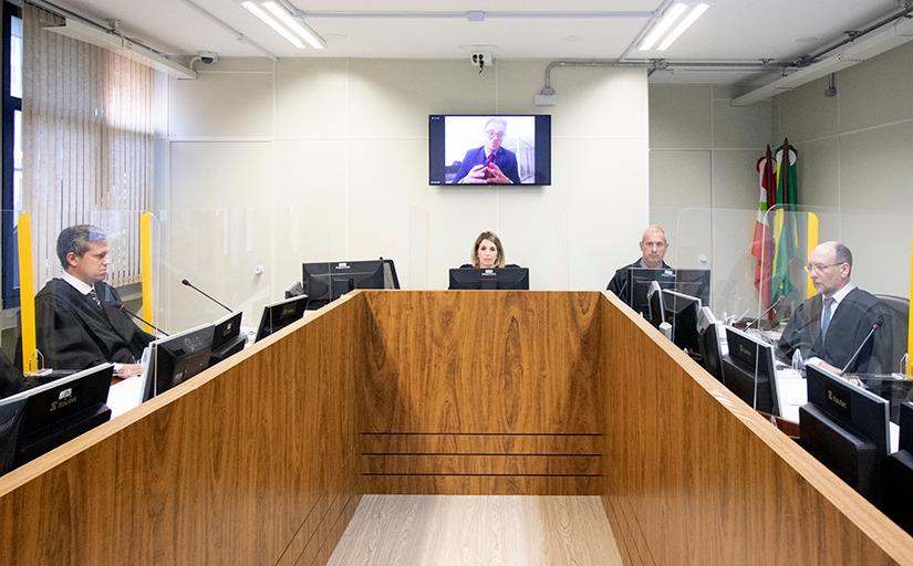 fotografia da sessão de julgamento. atrás de uma bancada de madeira, estão sentadas quatro pessoas, três homens e uma mulher. todos usam toga