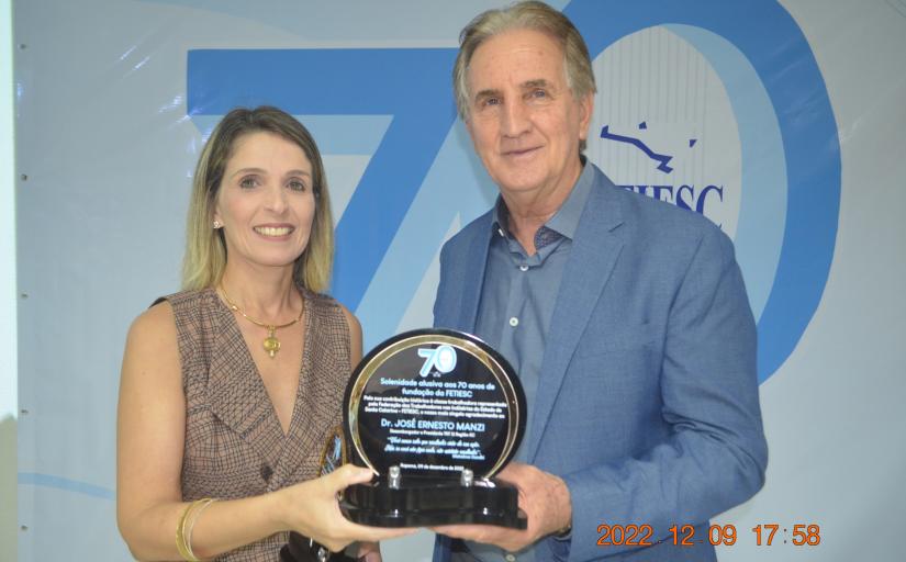 Foto de um homem e uma mulher sorridentes, lado a lado e  com um troféu na mão