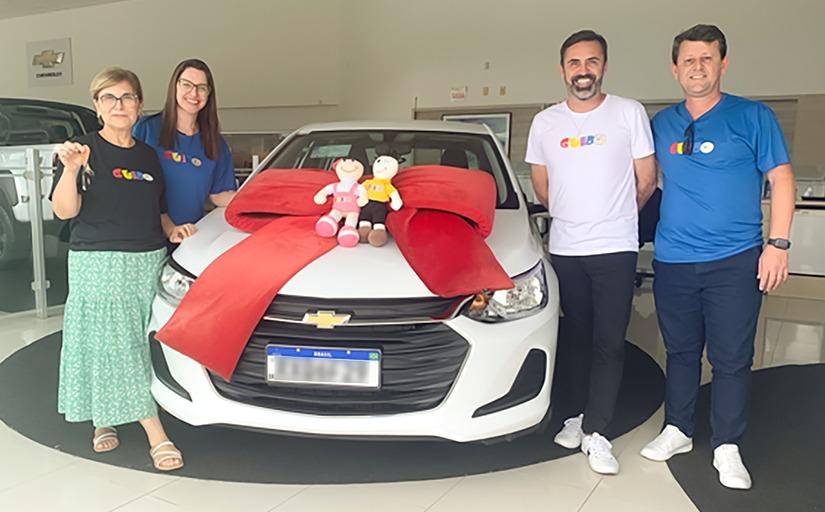 fotografia de quatro pessoas, dois homens e duas mulheres, em torno de um carro novo, em ambiente de concessionária