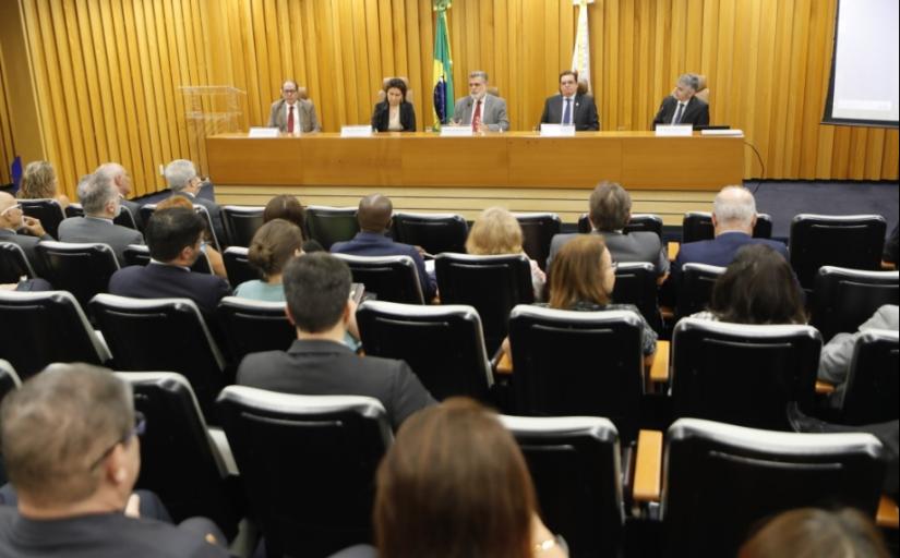 Foto tirada do fundo de um auditório mostra pessoas sentadas nas cadeiras e autoridades na mesa principal
