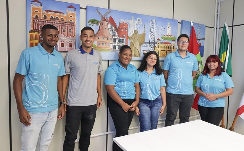 Três homens e três mulheres em pé, todos jovens, sorrindo e posando para foto