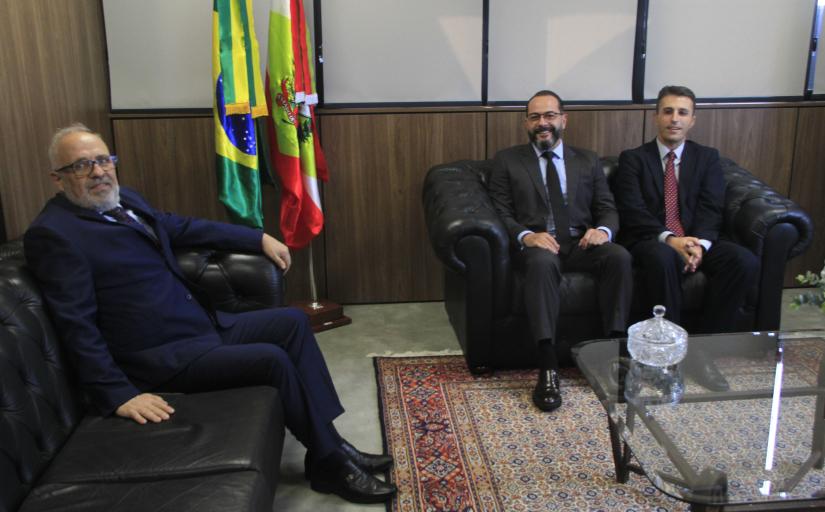 Três homens de terno escuro posam para a foto sentados em um sofá