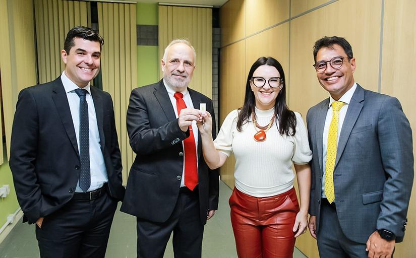 Foto de quatro pessoas, sendo três homens de terno e uma mulher. Um deles entrega uma chave para ela