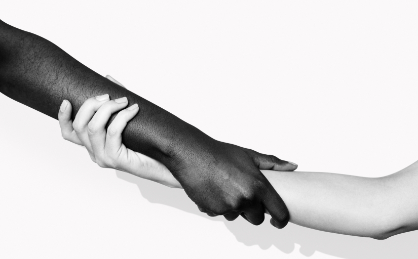 Dois braços, um negro e um branco, se entrelaçam, em foto preto e branco
