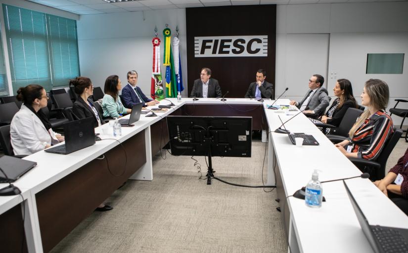 Fotografia de 10 pessoas reunidas em torno de uma mesa retangular olhando para o centro