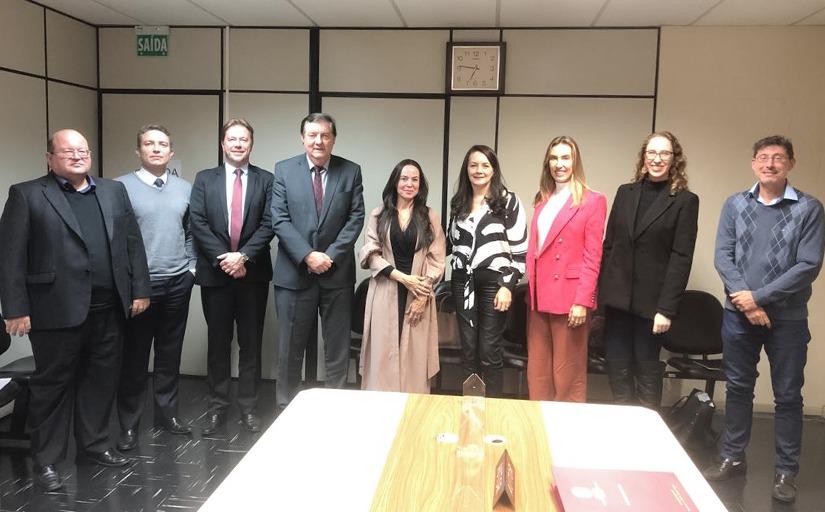 Cinco homens e quatro mulheres estão em pé, lado a lado, sorrindo e posando para a foto dentro de uma sala de reunião