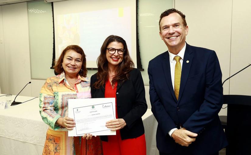 Foto de duas mulheres e um homem sorrindo. As mulheres seguram um documento.