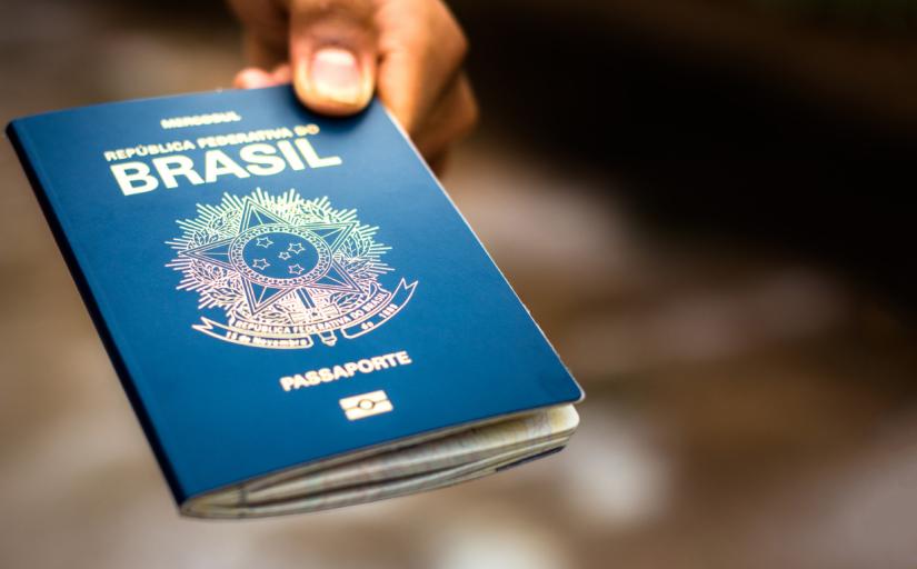 fotografia ilustrativa de uma mão negra segurando um passaporte brasileiro